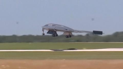A grey war plane as it lands on a runway in a green field
