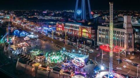 artist's impression of an aerial view of illuminated fairgrounds rides on Blackpool Promenade, in front of the Tower and its ballroom