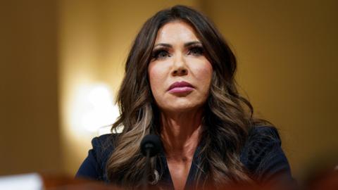 Kristi Noem attends a House Homeland Security hearing, she stares above the camera in a serious expression.