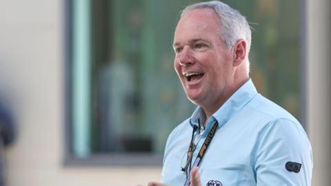 Tim Mayer smiling while wearing an FIA-branded long-sleeved shirt
