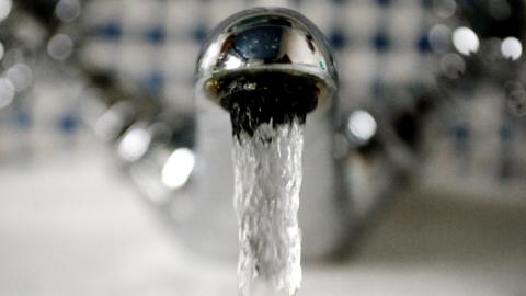 A close up of a silver-coloured tap with clear water pouring out of it.