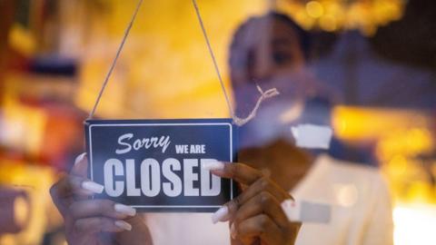 Woman putting closed sign on glass front door of coffee shop