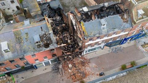 Gaping holes in roofs of terrace after fire - rubble from the building in centre spills on to the street.