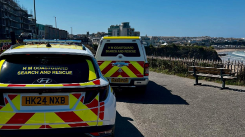 The picture shows two HM Coastguard search and rescue vehicles parked on a coastal road.