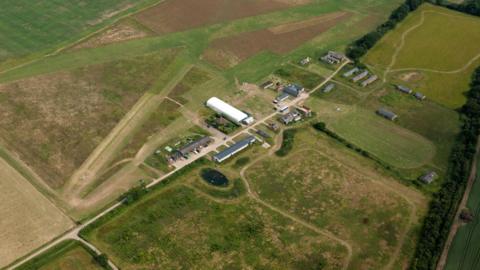 An aerial image of the Stow Maries Great War Aerodrome, which is made up of several buildings set on a large section of green land.