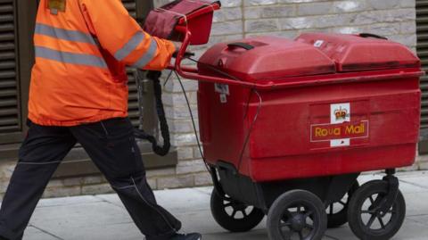 A post man wheeling a trolley full of letters.