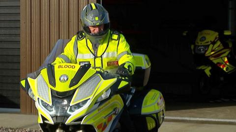 A south west blood bike rider sat on a motorbike in front of the charity's Devon headquarters in Plymouth