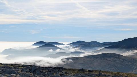 Mountain tops sandwiched between a thick layer of cloud below and a thinner layer above