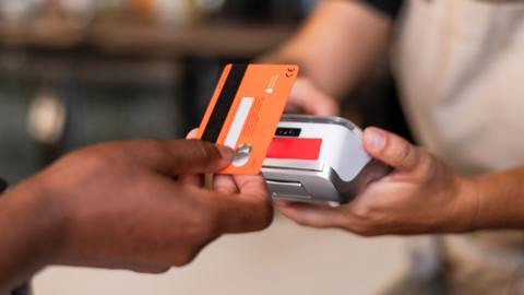 A hand tapping a card machine with a red credit card.