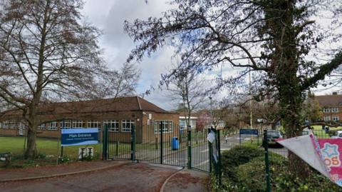 The main entrance to Warlingham School, with gates, railings and a blue sign.