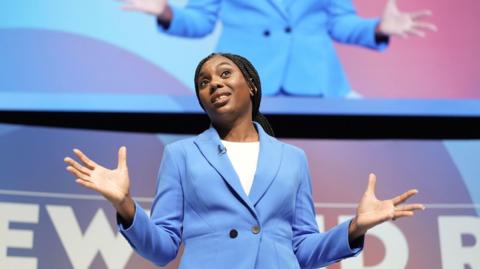 Kemi Badenoch wearing a blue jacket standing on stage at the Conservative Party conference this month . 