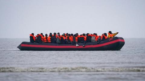 A group of of around 30 people wearing orange life jackets crammed onto a small boat in the English Channel