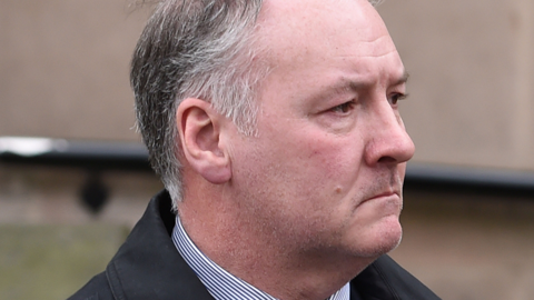 A man with grey hair and a white shirt and dark jacket