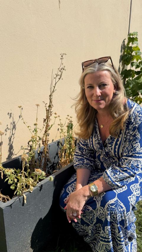 Woman dressed crouched down next to a plant which is dead.