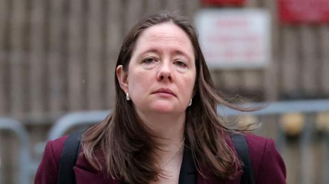 Maurene Comey wears a red jacket and has a blank expression