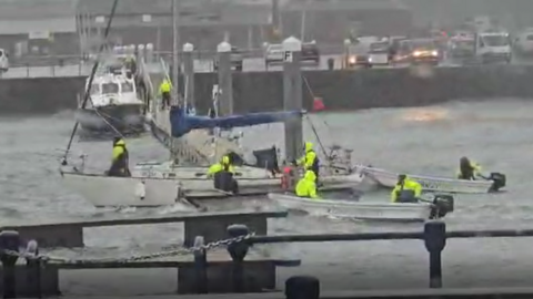 Boats in Victoria Marina rescuing a large sailing boat. There are three boats surrounding the vessel with people wearing hi-vis. 