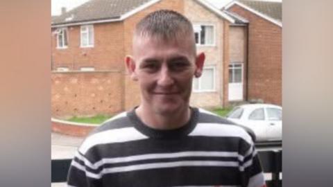 David Cuthbert. He is smiling at the camera and has short hair which has been shaved at the sides. He is wearing a black and white striped top.