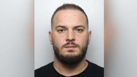 A mugshot of Alexandru-Daniel Iarcu, who has a beard and short, dark hair. He is wearing a black shirt.