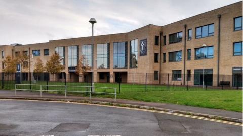 The outside of Caldicot School in Monmouthshire. A beige bricked three-storey building with a flat roof and large glass windows. There are some small tress outside and some grass