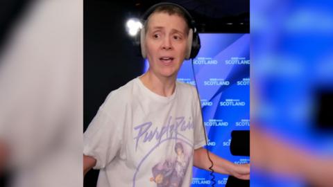 Woman in a white Prince T-shirt dancing in a blue radio studio with headphones on.