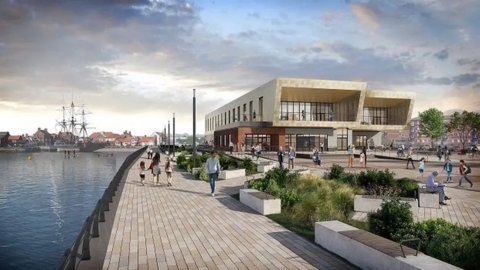 An image of what Highlight, the new leisure facility next to Hartlepool Marina, might look like. It is a modern beige building with garden features outside and lots of seating. A river flows alongside the leisure centre.