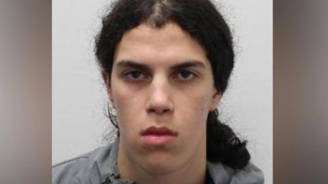 Zachariah Boulares - a young man with long, curly dark hair tied back