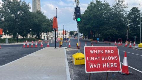 A sign reading "when red light shows wait here"  placed on a central lane of Cumberland Place, Southampton with a temporary traffic light showing green. Bollards line the road to close off the lane to traffic.