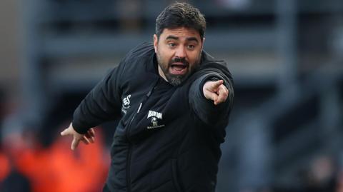 Vitor Matos wearing black Swansea jacket points towards camera