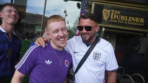 A Scotland and an England fan wearing their team jerseys laugh together