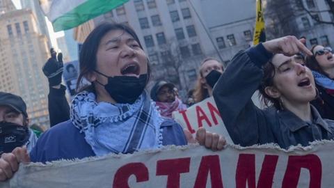 Protesters shout as they hold signs and wave Palestinian flags