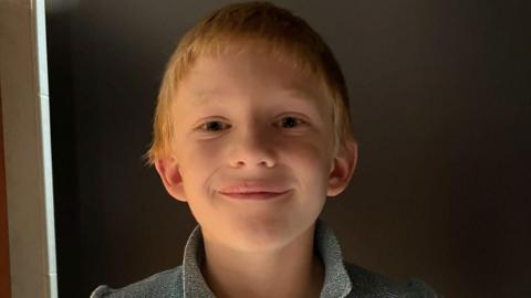 Zac with blonde hair smiling at the camera