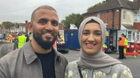 Ahmed (L) and Rifat Ali (R). They are wearing grey clothes and are stood in front of workmen in a street.