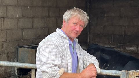 Andrew Bebb, wearing a white checked shirt, leaning on a metal farm gate