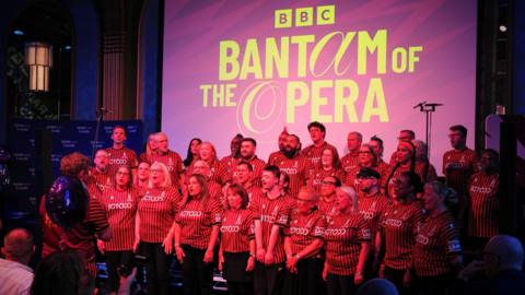 People wearing Bradford City tops singing in a choir. A large purple sign behind them reads: "BBC Bantam of the Opera."