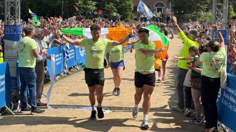 two men in t shirts and shorts run under an arch