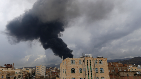 A large plume of black smoke rising behind a red-bricked building in Sanaa, one of may including blocks of flats