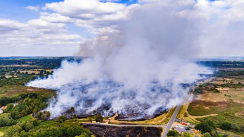 White plumes of smoke swirling into the sky, fields a seen in the foreground.