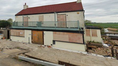 Roadside view of the derelict building of the pub with a red roof