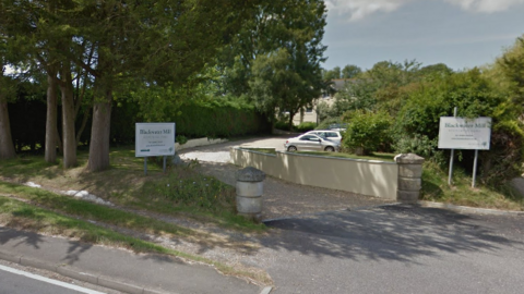 Exterior view of Blackwater Mill Residential Home - a white two-storey building at the end of a curved drive, with trees and a hedge to the left