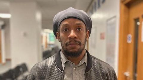 Jukome from the shoulders up. he is a black male, and is wearing a black leather jacket. The background is out of focus.