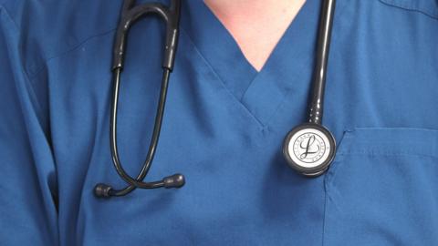 A close up of a person in blue scrubs, showing their chest area. They have a stethoscope around their neck.