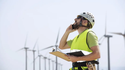 Man wearing a hard hat stood close to wind turbines