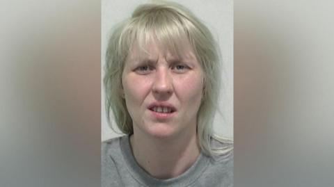 Mugshot of Peel. She has shoulder length white blonde hair and her face is fixed in a slight scowl.