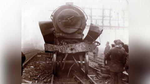 A black and white picture of one of the steam locomotives in the aftermath of the crash. Much of the metalwork at the front is mangled.