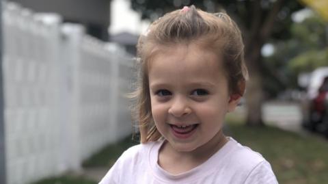 Family photo of five-year-old Ava Begley, wearing a pale pink T-shirt and smiling 