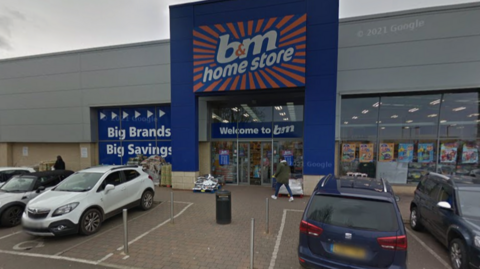 A close up of the front of the B&M store in Stevenage with its colourful signage. It is a grey day.