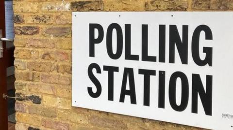 Plain black and white Polling Station sign against a brick wall