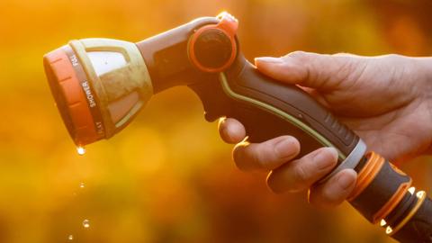 An orange tinted image of a hand holding a garden hose with water droplets dripping from it. 