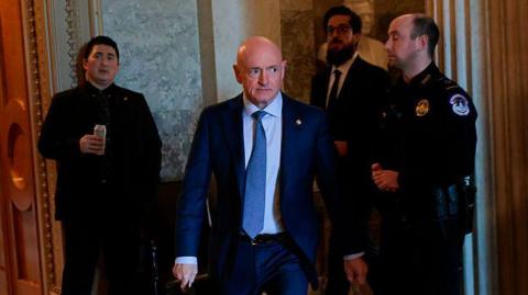 US Senator Mark Kelly seen walking through the halls of Congress, flanked by police and staff