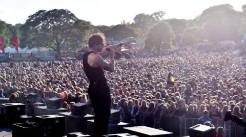 Tom Grennan performs at Radio 1's Big Weekend on Saturday 27 May 2023. He is standing on stage singing into a microphone in front of a vast sea of people below him.
